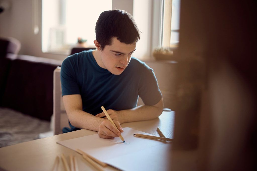 Man with down syndrome drawing on the paper at home.