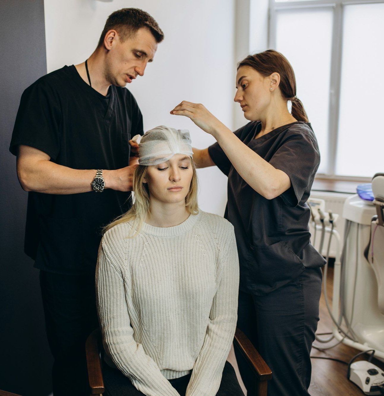 Two doctors bandage the head of a beautiful woman after plastic surgery